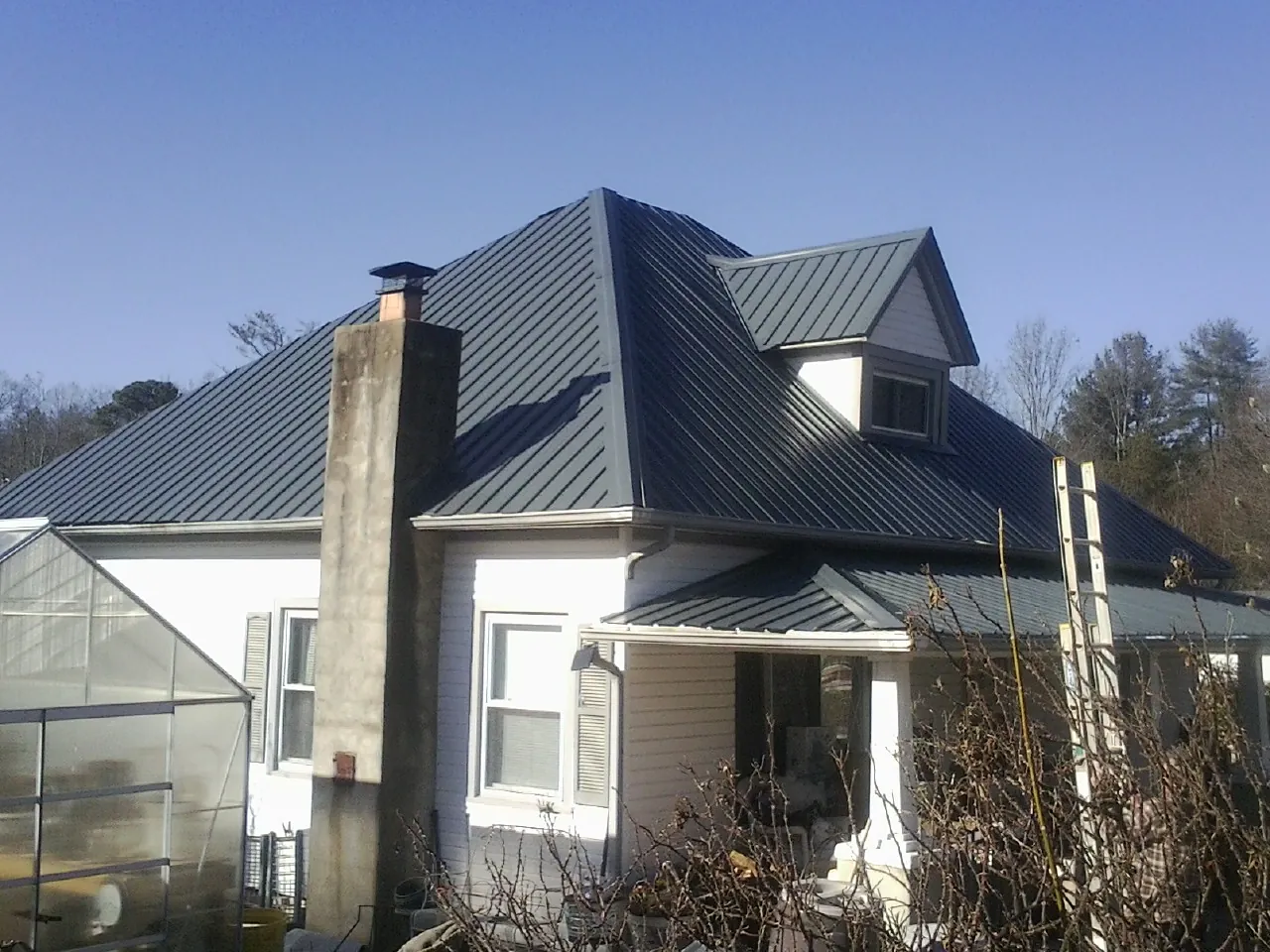 Dark blue standing seam metal roof on a white farmhouse with dormer — Slate & Tile Roof Repair by Roofing Brothers in Keno