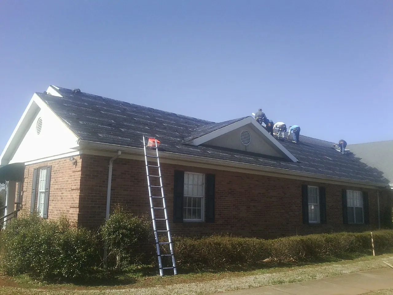 Crew tearing shingles off a brick ranch roof with a ladder set — Emergency Roof Repair work by our crew in Keno