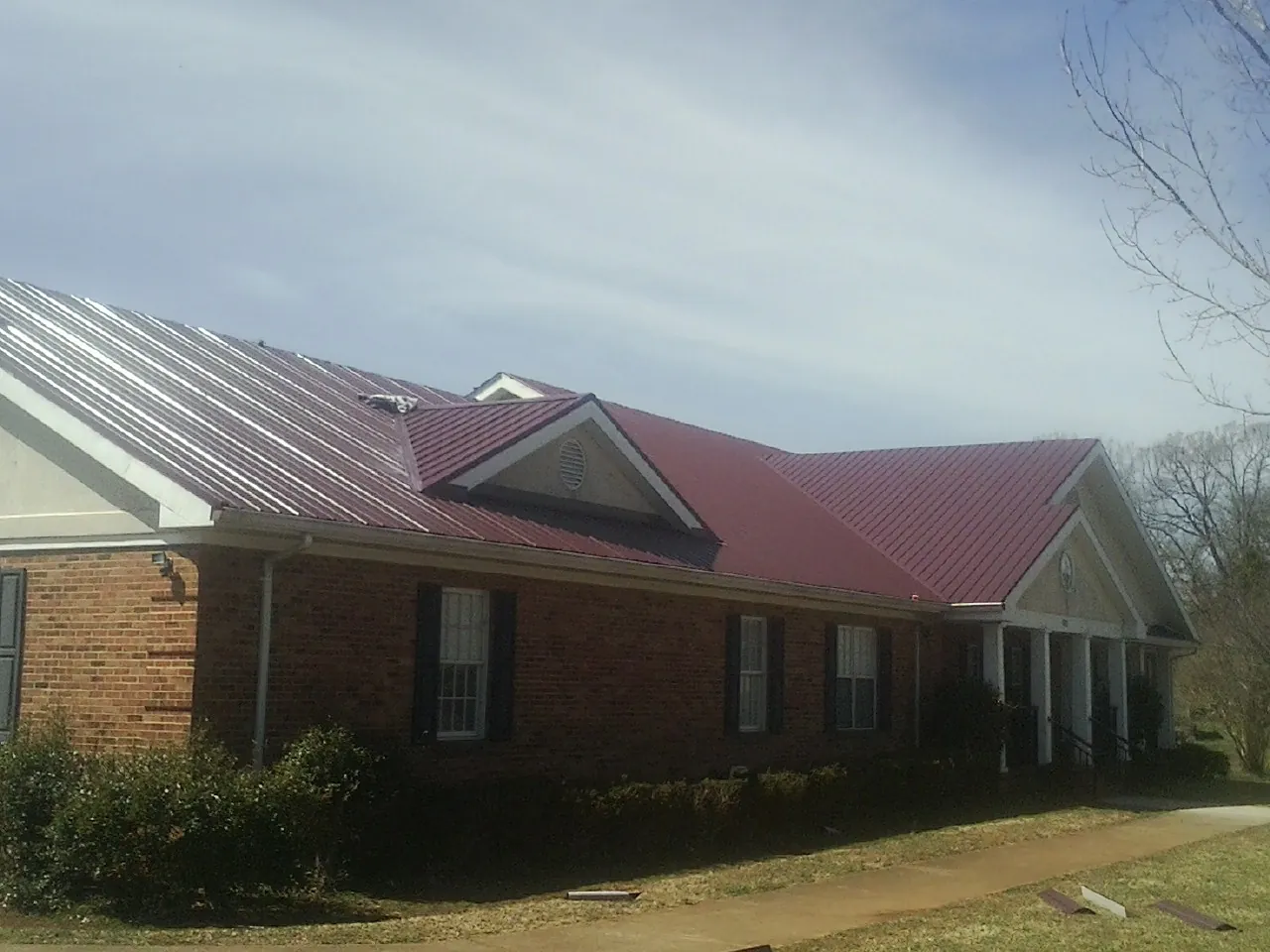 Red metal roof with gabled entries on a long brick building, from a Hail Damage Roof Repair job in Keno