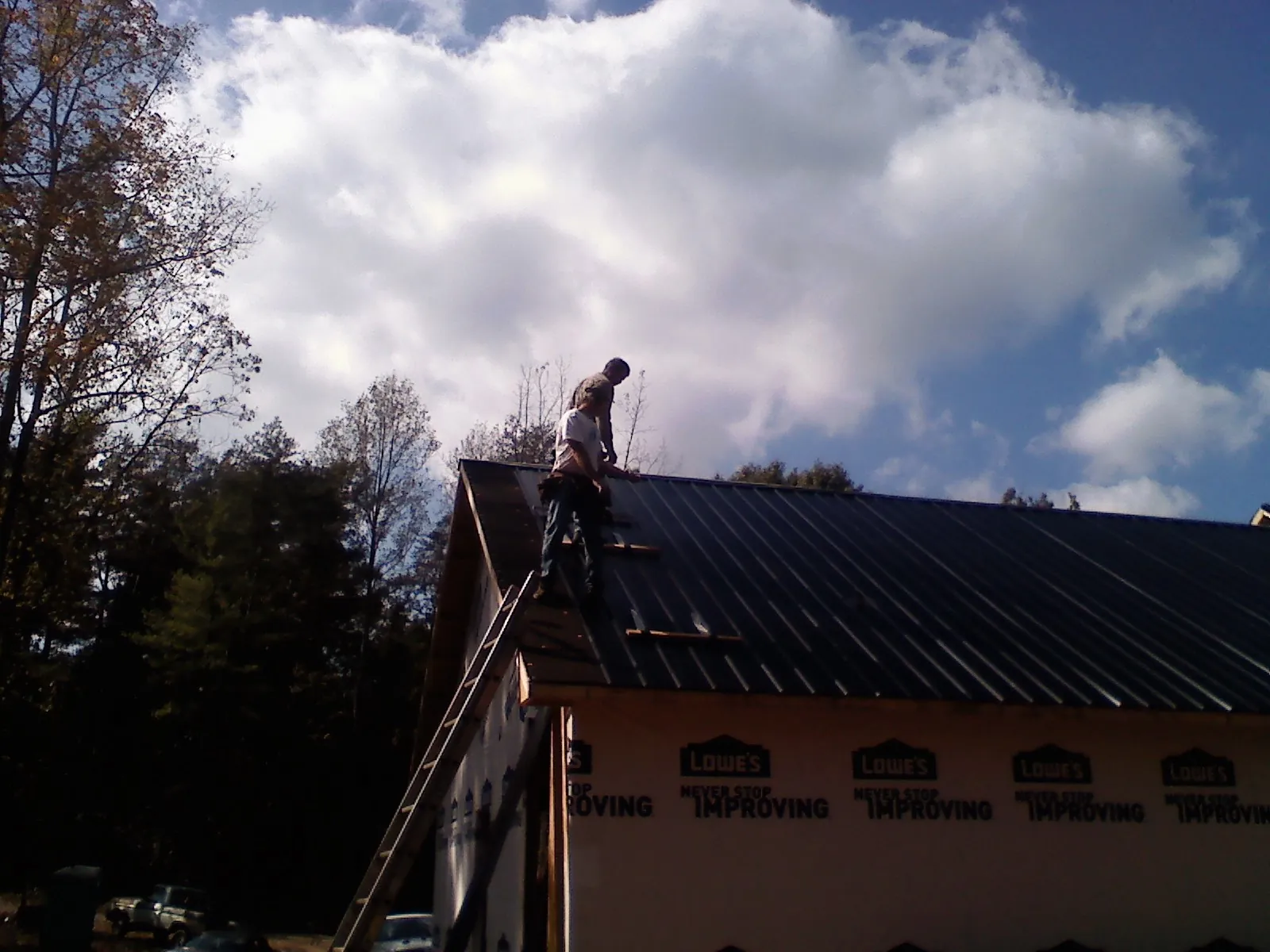 Roofer fastening dark metal panels high against a cloudy sky, from a Roof Inspection job in Keno