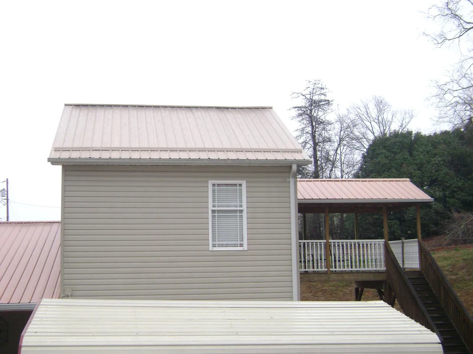 Tan metal roofs on a two story addition and attached porch, from a Roof Replacement job in Keno